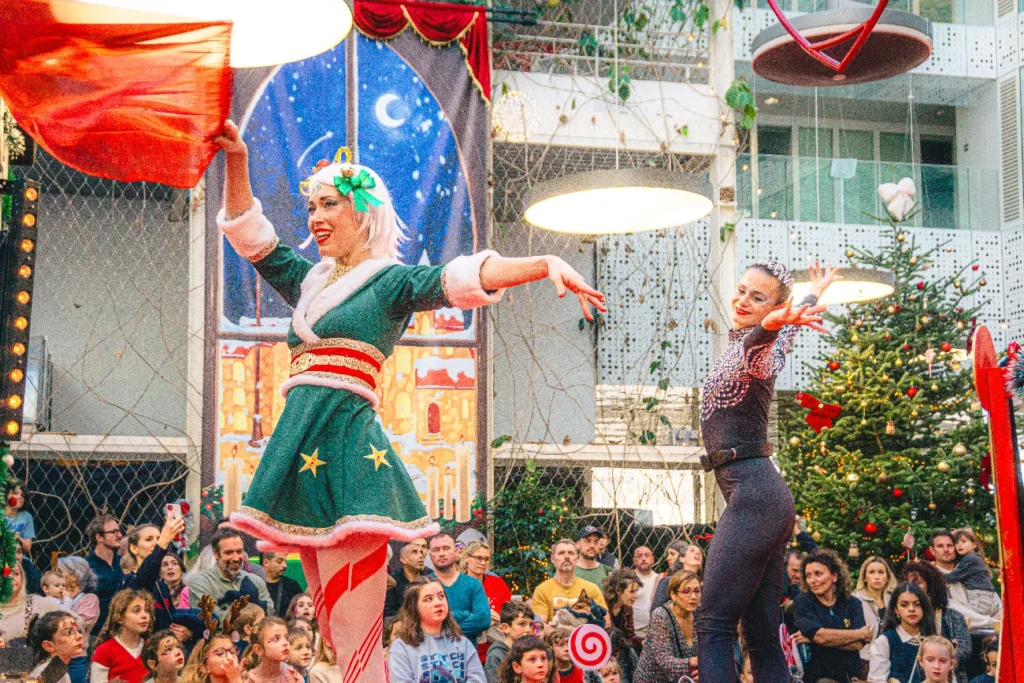 Artiste en costume vert et rouge de Noël perchée sur une structure lors d'un spectacle en intérieur devant un public